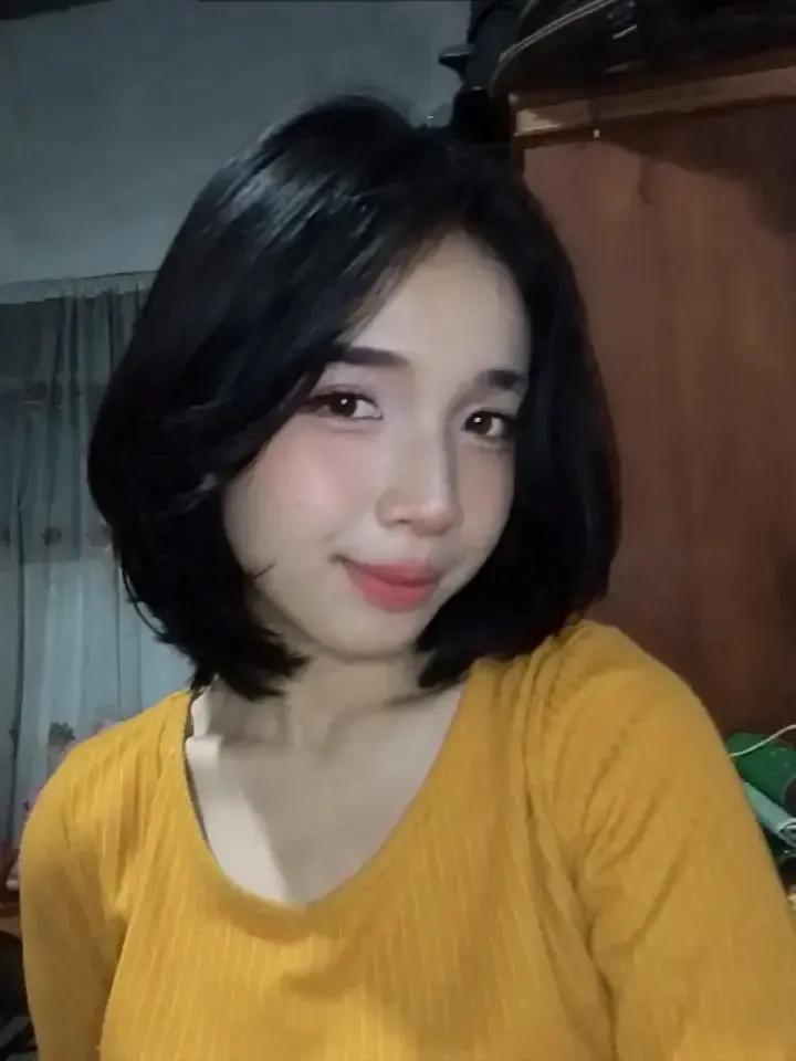 Yarin smiling at the camera, with her glossy black bob haircut and a mustard yellow sweater
